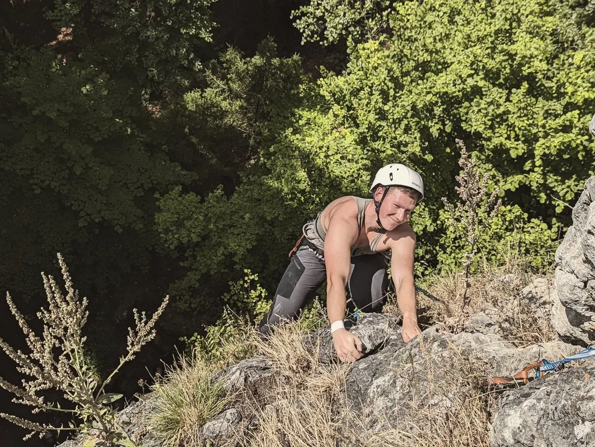 Gerome mit Helm klettert über einen bewachsenen Felsen